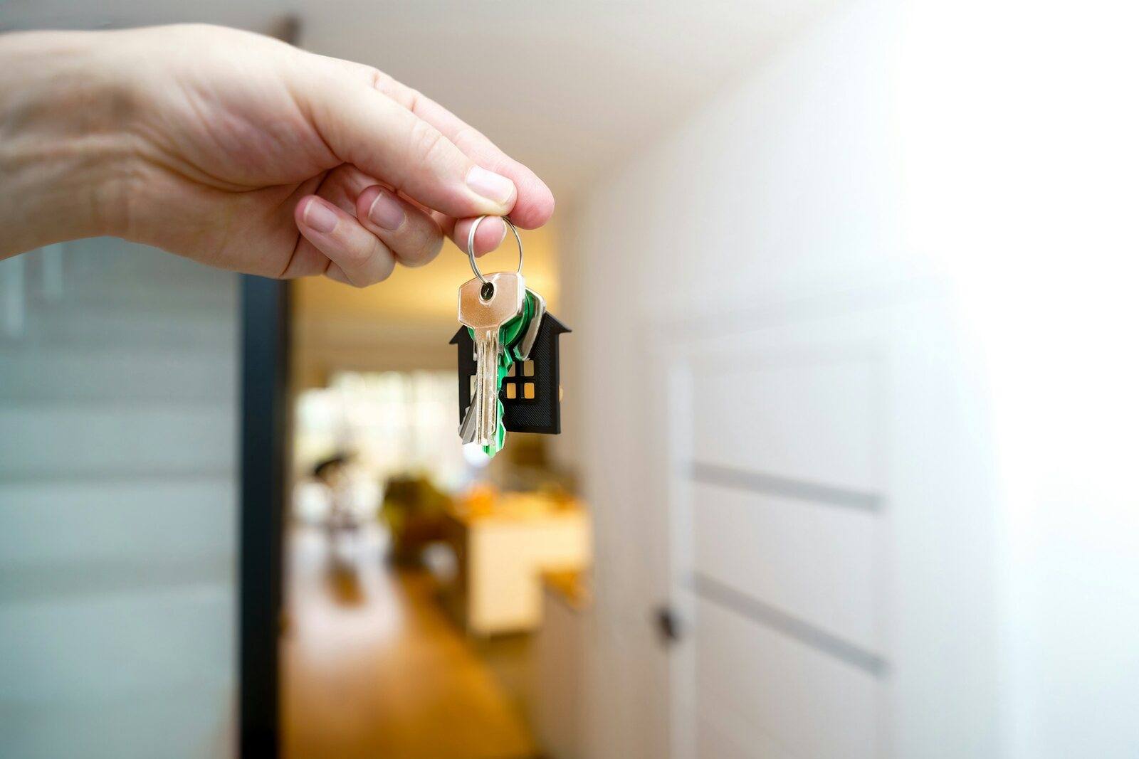 Eine Hand hält einen Wohnungsschlüssel mit Anhänger in Hausform.